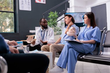 Hastane resepsiyonunda muayene sırasında kırık olan yaralı hastanın boyun tasmasını çıkarıyorlar. Hemşire ve sıhhiye Asyalı genç adama, sağlık hizmetlerine destek veriyor.