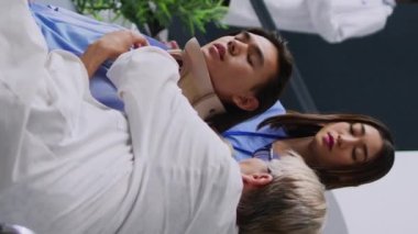 Dikey video: Başhekim hastanenin bekleme salonunda yaralı hastaya boyun tasmasını çıkarması için yardım ediyor. Sonra Asyalı bir adamla sağlık uzmanlığını tartıştılar.