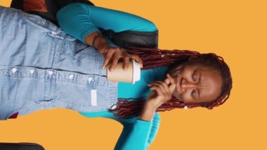 Dikey video: Yorgun bir kadın kahve fincanı içiyor ve kamera önünde esniyor, uçakla tatile çıkmaya hazırlanıyor. Tatilde seyahat etmekten yorgun düşmüş, kafein içen bir kadın..