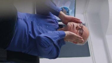 Dikey video: Hastane resepsiyonunda oturan stresli yaşlı hasta, sağlık muayenesi sırasında uzman doktorun tıbbi muayeneye başlamasını bekliyor. İlaç servisi ve...