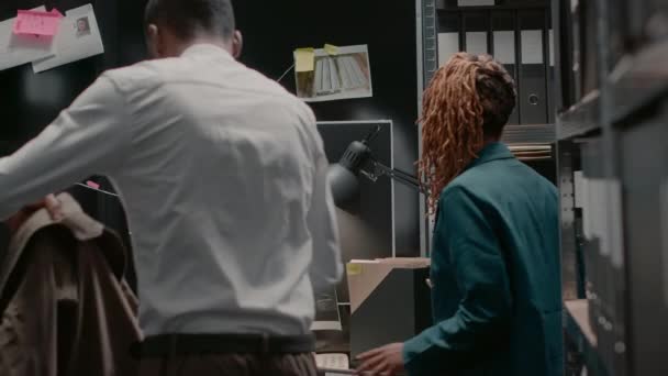 非裔美国警察小组阅读案件线索 在私人证物室与侦探地图合作解决犯罪问题 两名视察员正在审查监视照片 以发现细节 手持射击 — 图库视频影像