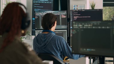 Veritabanı programcısı terminal penceresine ajans ofisindeki birden fazla monitörü kullanarak kod yazıyor. Sistem yazılım geliştiricisi veritabanı bilgisini yazıyor, büyük veri betiği hesaplanıyor.