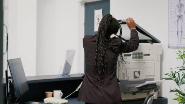 Medical employee working at hospital reception desk, using landline phone to make checkup appointments with patients. Facility worker planning healthcare consultations at counter. Handheld shot.