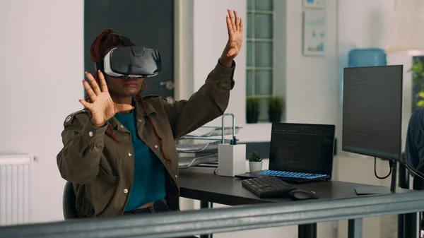 Vista lateral de la mujer con el pelo rojo con gafas de realidad virtual  mientras juega videojuegos con controlador inalámbrico.