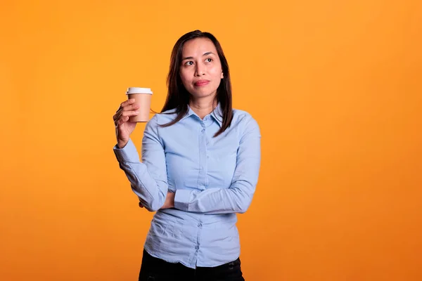 无忧无虑的亚洲女人在工作室里享受着热卡布奇诺饮料 摆出黄色的姿势 在休息时间举杯咖啡 微笑的自信模式享受小食饮料 — 图库照片