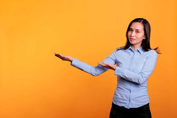 正面的模式指向工作室广告促销产品 广告理念 笑容可亲的菲利皮诺女人站在黄种人的背景上 做广告做手势 — 图库照片