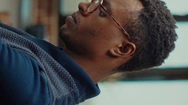 Dikey video: Erkek çalışan iş geliştirme üzerinde çalışmak için vizyon düşünüyor, birlikte çalışma alanında dizüstü bilgisayar ve belgeler kullanıyor. Afrikalı Amerikalı önemli kurumsal bilgileri okuyor..