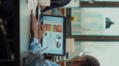 Dikey video: İş dünyası ekibi toplantı odasında yeni stratejileri tartışıyor, dizüstü bilgisayardaki veri analizlerine bakıyor. Belgeler raporlarına göre, başlangıç geliştirme çözümleri bulmak için beyin fırtınası fikirleri.