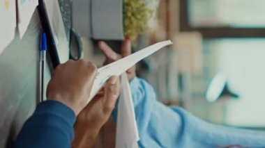 Dikey video: İş ortakları planda işbirliği yapıyor, yeni şirket vizyonu yaratmak için ofisteki araştırma belgelerine bakıyorlar. Geliştirme stratejisi için analitik ve sonuçlarla çalışmak, başlangıç