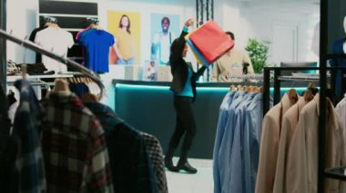 Asyalı alışverişçi alışveriş merkezinde alışveriş yaparken, kasadan alışveriş torbalarını aldıktan sonra dans ederken mutlu hissediyor. Moda dükkanında dans figürleri gösteren genç bir müşteri. El kamerasıyla..