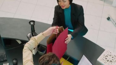 Asyalı müşteri alışveriş torbalarıyla perakende mağazasından ayrılıyor, alışveriş merkezindeki butikten moda kıyafetler alıyor. Genç bir kadın kasadaki postal terminalini kullanıyor, ödeme yapıyor. El kamerasıyla..