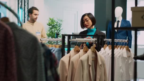 不同的女人看着架子上的商品 顾客试图购买新的现代服装 年轻的购物者看着衣架上的正式服装 与零售精品店的店员交谈 — 图库视频影像