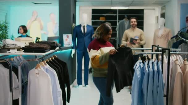 服装店的工作人员帮助顾客选购服装 为他们购买新的时尚服装 在精品店里与购物中心员工谈论时尚商品的年轻女人 — 图库视频影像