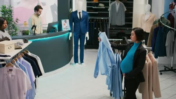 ラック上の新しいファッションコレクションを見て モールで衣料品店での正式な摩耗のためのベビーバンプショッピングを持つ女性のクライアント 妊娠中の将来の母親はショッピングセンター 商業活動を訪問 — ストック動画