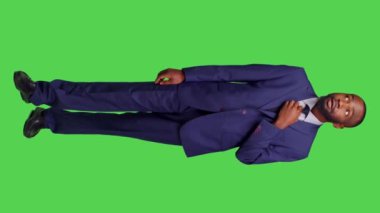 Dikey video: Afrika kökenli Amerikalı iş adamının şaşırdığını, stüdyoda yeşil perde arkaplanı ile şok etkisi yarattığını gösteren ön görüntüsü. Takım elbiseli bir erkek kamera karşısında şaşkına dönüyor.