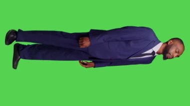 Dikey video: Stüdyoda imza attığını ve yeşil ekranda poz verdiğini bilmediğim genç işadamının yan görüntüsü. Erkek şirket yöneticisi ofis kıyafeti giyiyor. Kafası karışık ve kararsız.