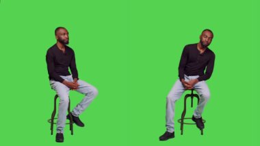 Sandalyede kendine güvenen Afro-Amerikan bir adam, yeşil perde arkasında oturuyor. Genç erkek model kendini iyimser hissediyor ve stüdyoda bir şey bekliyor, doğal insan..