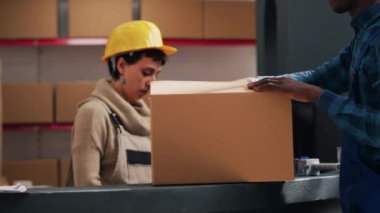 Genç depo çalışanı paketlere yapışkan bant yapıştırıyor, depo alanında ürünlerle birlikte sipariş hazırlıyor. Erkek müfettiş karton kutuları mallarla, teslimat servisiyle kapatıyor..