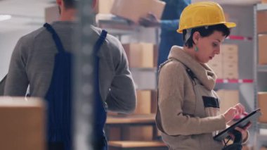 Depodaki ürünleri tarayan genç işçiler, barkodları ve lojistiği kontrol etmek için dijital tablet ve tarayıcı kullanıyorlar. Stok envanteri ve sanayi departmanı planlayan bir ekip..