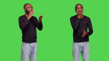 Kotlu genç adam stüdyodaki insanlara hava öpücüğü veriyor, yeşil ekranda öpüşen yüzüyle poz veriyor. Romantik jest yapan, çapkın, kendine güvenen bir erkek manken..