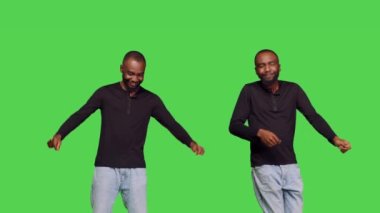 Rahatlamış oyuncu kamera önünde dans hareketleri yapıyor, etrafta takılıyor ve yeşil ekran arkaplanı üzerinde aptalca davranıyor. Genç erkek model neşeli ve komik. Stüdyoda eğlence olsun diye dans ediyor..