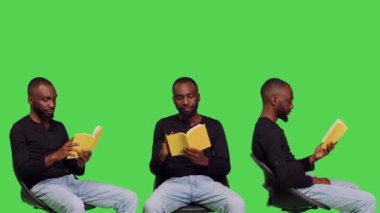 Afrikalı Amerikalı bir adam romandan büyüleniyor, stüdyoda sandalyede edebiyat kitabı okuyor. Erkek model kendinden emin ve yeşil ekran arka planında poz veren hikayeden zevk alıyor..