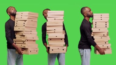Afrika kökenli Amerikalı bir adam elinde pizza kutularıyla yeşil ekranın arkasına yığılmış bir şekilde stüdyoda hazır yemek siparişi taşıyordu. Erkek model paket servis elemanı olarak çalışıyor..