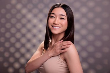 Asyalı güzellik modeli gülümsüyor ve omuz portresi üzerinde el ele tutuşuyor. Yüzü pozitifken çekici bir kadın kendine güvenen modaya uygun bir şekilde duruyor ve çıplak doğal makyaj yapıyor.