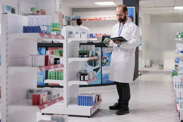 药师穿着白衣 在药店的设备上看药丸包装上的库存药品 药房是高质量和有效的药物和治疗选择的可信赖的来源 — 图库照片