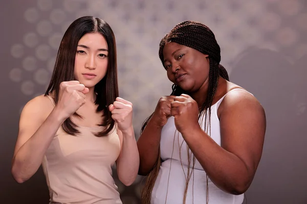 African american and asian women standing in fighter pose, demonstrating girls power. Strong diverse models with different body shapes and ethnicity fighting and showing fists