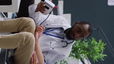 Dikey video: Travmatolog Asyalı hastada hipertansiyon ve hipotansiyon ölçüyor, yüksek veya düşük nabız basıncını ölçmek için tıbbi tonometre kullanıyor. Doktor enstrüman ile genç yetişkinlere danışmak