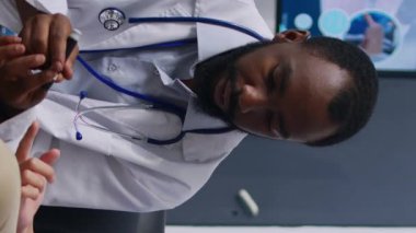 Dikey video: Kan örneğinden alınan insülin ve glikoz seviyesini ölçen glukometresi olan Asyalı bir hastaya danışmanlık. Doktor ve genç yetişkin check-up sırasında diyabetik kontrol yapıyorlar.