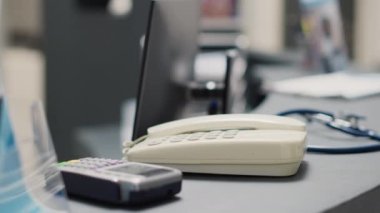 Hastane lobisinde tıbbi randevuları, kayıt formlarını ve tıbbi broşürleri kaydetmek için kullanılan sabit hatlı telefonu olan boş bir resepsiyon. Kablosuz telefonlu teşhis merkezi sayacı. Kapat..