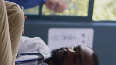 Dikey video: Şeker seviyesini kan örneğiyle ölçen uzman, diyabetli Asyalı hastaya tıbbi glukometre ile insülin testi yapacak. Afrika kökenli Amerikalı doktor muayene sırasında glikozu kontrol ediyor.
