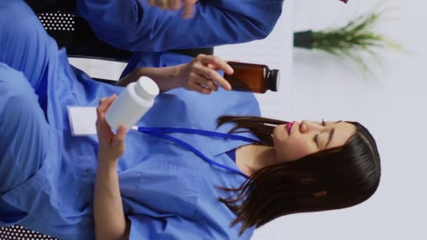Вертикальне Відео Азіатська Медсестра Показує Пляшку Таблетками Літньому Пацієнту Обговорюючи — стокове відео