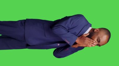 Dikey video: Stüdyoda esneyen ve yorgun hisseden genç yetişkin görüntüsü, uzun bir iş gününden sonra hayal kırıklığına uğruyor ve yoruluyor. İş adamı uykuya dalıyor ve bitkin düşüyor, yeşil ekran