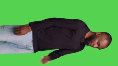 Dikey video: Erkek modelin, izole edilmiş yeşil ekran arkaplanındaki bilgileri düşünceli ve bekleyerek düşünceli bir şekilde düşünmesi. Sabırlı genç adam yeni fikirler üretiyor.