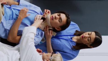Dikey video: Hastane bekleme odasında sağlık görevlisi yaralı hastaya muayene sırasında boyun tasmasını çıkarmasında yardım ediyor. Boyun yaralanması geçiren Asyalı bir adam tıbbi yardım alıyor