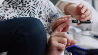 Dikey video: Yaşlı doktor hastane resepsiyonunda glukometre kullanarak insülin seviyesi testi yapıyor, hastanın kan örneğinden glikozu ölçmek için diyabet muayenesi yapıyor. Son sınıf öğrencisi check-up yaptırıyor.