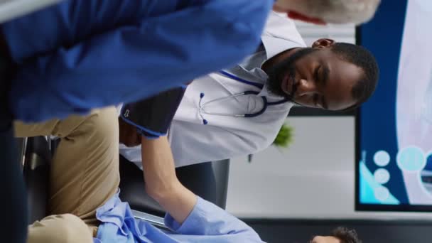 垂直ビデオ 医師は病院の待合室で予約を訪問中に糖尿病患者を助けるために医療機器でインスリンレベル測定を行う 医療支援 — ストック動画