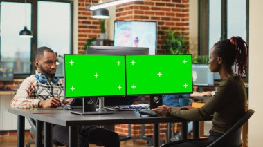 Afrika kökenli Amerikalı kadın monitörlerde yeşil ekran görüntüsü kullanıyor, ofiste boş model şablonuyla çalışıyor. PC üzerinde izole edilmiş telif alanı ve krom anahtar ekranına bakan kadın çalışan.