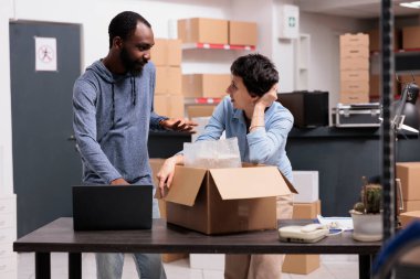 Depo çalışanları, müşteri paketini karton kutuya koyduktan sonra ambalaj paketine koyduktan sonra nakliye lojistiğini tartışıyor. Depodaki ticari taşımacılıkta çalışan çeşitli çalışanlar
