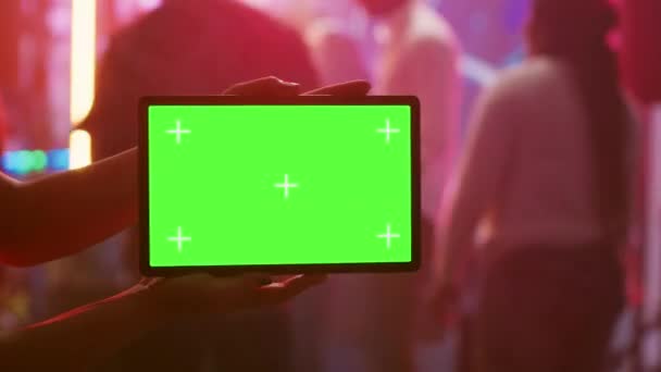ナイトクラブで緑の画面を持つタブレットを示す人は モックアップテンプレート付きのダンスフロア保持デバイスにあります 女の子見ますで隔離されたクロマキーディスプレイとともに空白のコピースペース — ストック動画