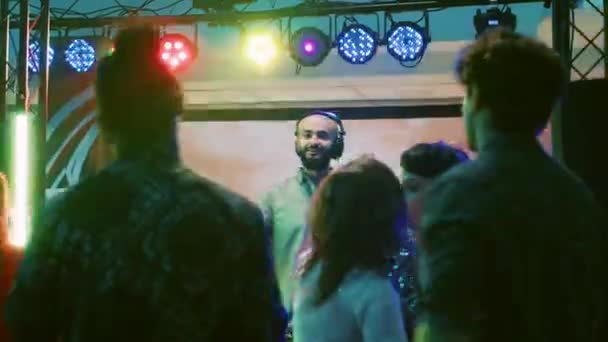 男性Djはクラブパーティーで音楽を入れ オーディオ機器ステーションで電子サウンドをミックスします ダンスフロア クラブエンターテイメントで飛び回って踊る多様な友人のグループ — ストック動画