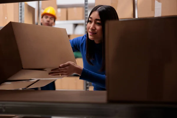 Logistics manager doing goods parcels quality control while searching cardboard boxes on shelf. Ecommerce retail storehouse employee holding package to pack customer order for shipment