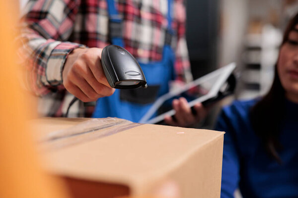 Retail storehouse employees doing inventory management while scanning packages. Postal service warehouse manager holding barcode scanner and digital tablet in arm close up