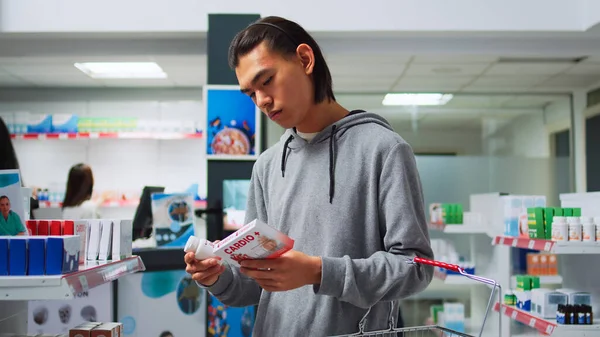 男性顾客在看从药店购买的心脏科药物 试图治愈心脏问题 年轻人阅读药丸和维生素的包装 提着装有药品的篮子 — 图库照片