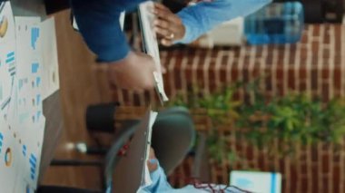 Dikey video: Yönetim kurulu toplantısında belgeleri inceleyen şirket çalışanları, tabletle yıllık veri sunumu üzerinde çalışıyorlar. Meslektaşlar iş uzmanlığı planıyla karı artırmaya çalışıyor.