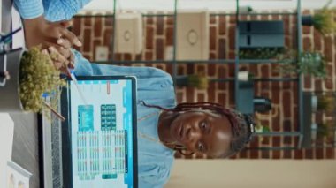 Dikey video: Başlangıç çalışanı dizüstü bilgisayarda yönetici raporu gösteriyor, kâr geliştirmek için çevrimiçi analizleri inceliyor. Çalışanlar grubu, belgelerle ilgili yeni veri raporunu tartışmak için toplantı odasında toplandı..