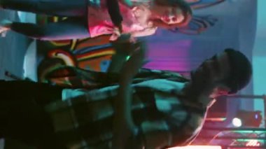 Dikey video: Genç yetişkinler eğleniyor, dans ediyor ve dans pistinde sahne ışıklarıyla dolaşıyorlar. Eğlenceli dans hareketleri yapan neşeli arkadaşlar yeraltı partisinde eğleniyorlar. El kamerasıyla..